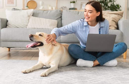 Women sitting on the floor petting a yellow lab while working on a laptop