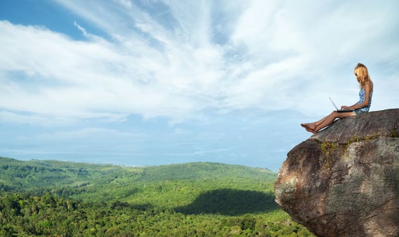 Remote worker sitting on a rock with a laptop