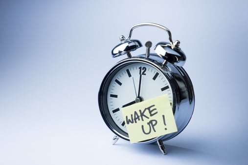 Concept of the idea of a wake up call. An alarm clock with a post-it that says wake up. 