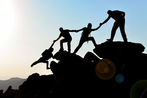 A group of four people helping each other over rocks