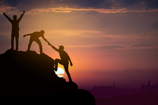 Three people helping each other climb to the summit of a mountain against the backdrop of a sunset. 