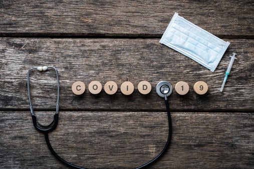 Letters spelling out the word COVID-19 on a wooden background with a mask and stethoscope 